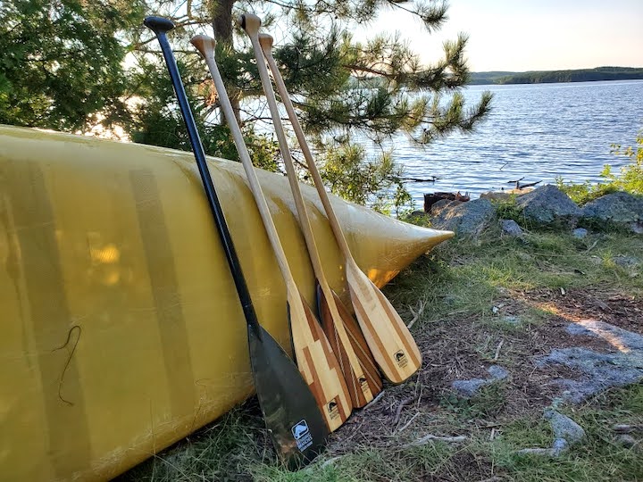 four canoe paddles leaning against a yellow canoe next to a lake