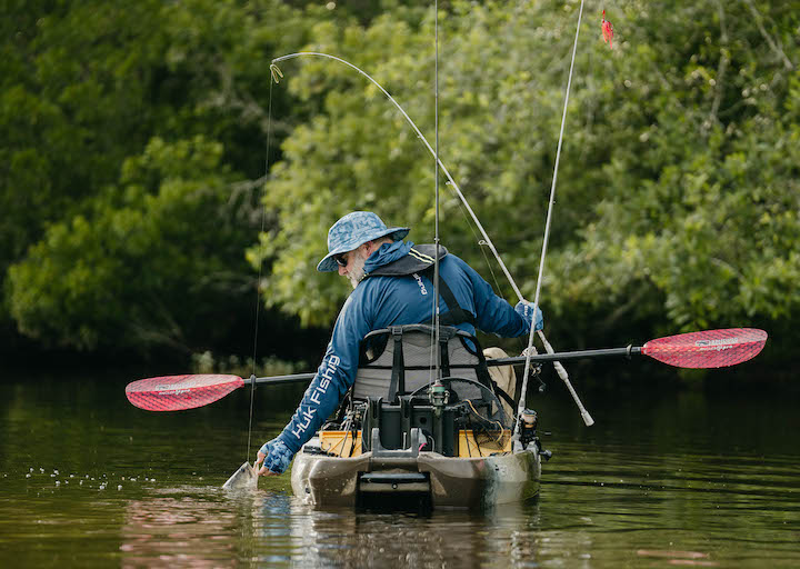 man releasing a fish back into the water in his fishing kayak