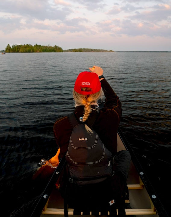 a woman paddles a canoe at the bow on a wilderness lake
