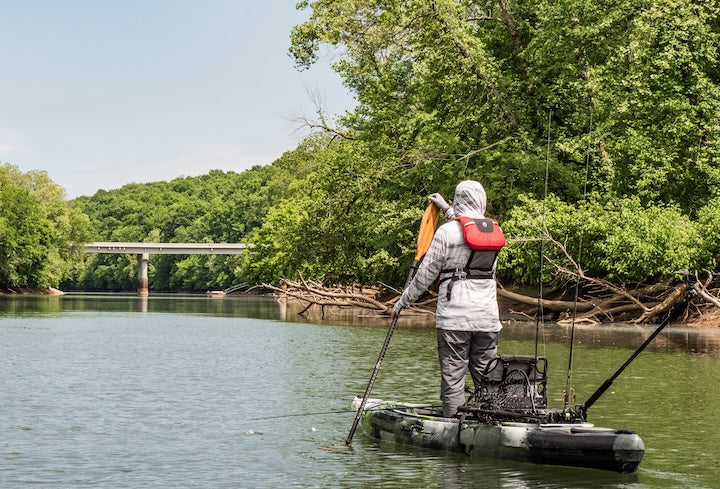 a kayak angler paddles while standing in his kayak on a slow river