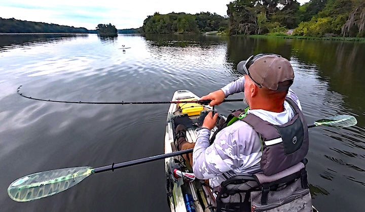 a man fishes from his kayak on a lake, cradling his Bending Branches paddle on his lap