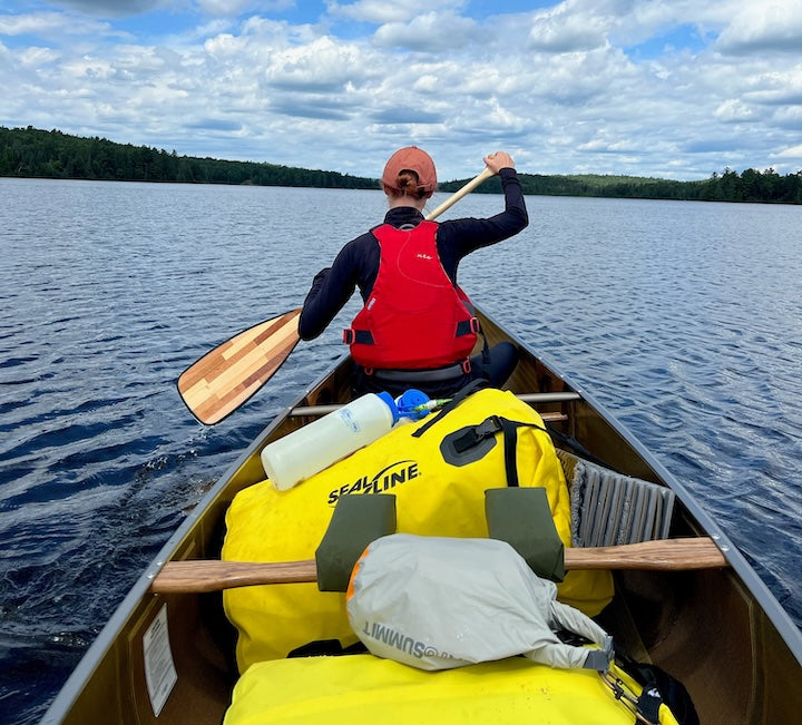woman in canoe bow paddles in a loaded canoe